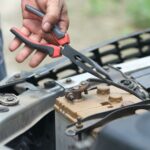 Hånd holder en tang over bilbatteriet i et åpent motorrom